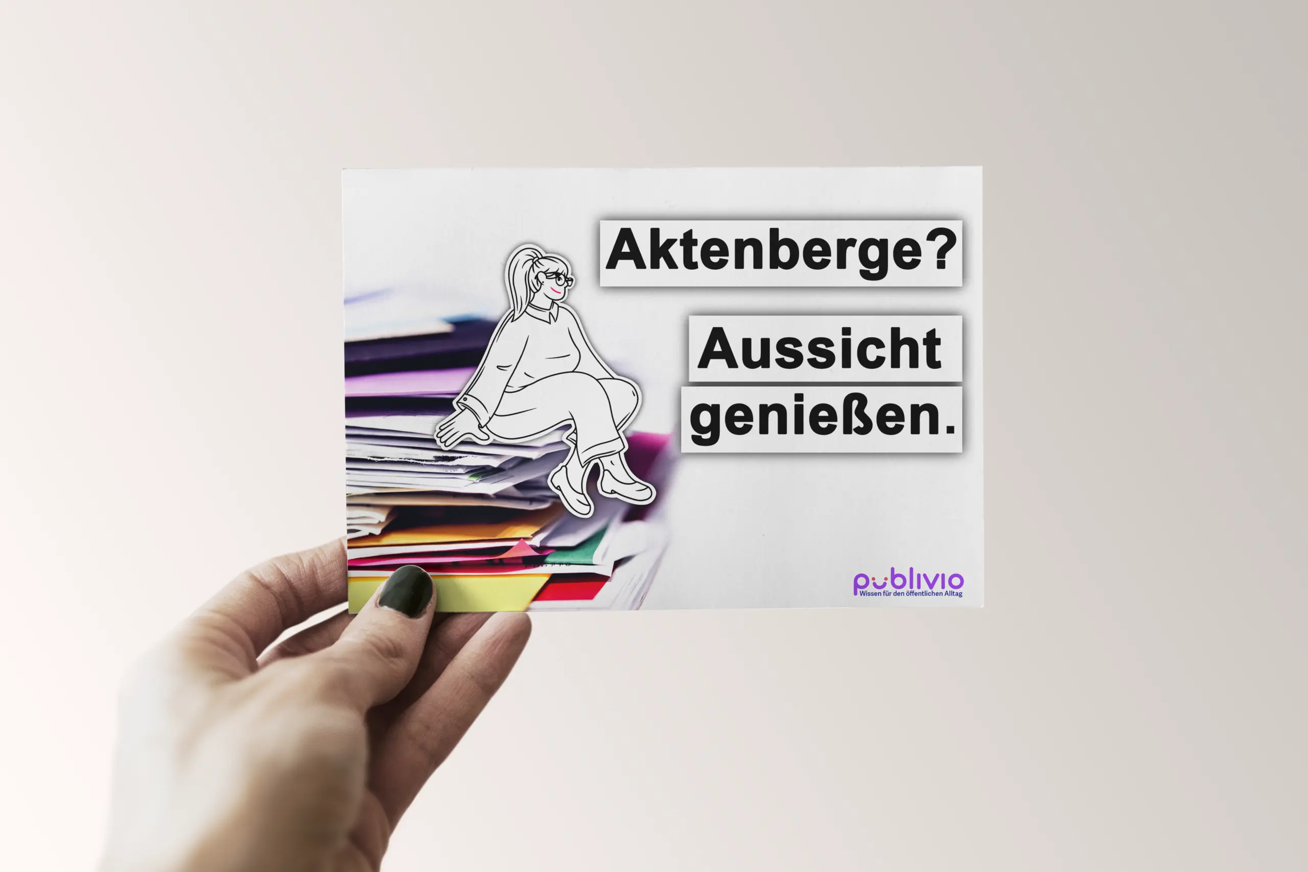 Postkarte Homepage Eine Hand hält eine Postkarte vor einem hellen Hintergrund. Auf der Karte ist eine Illustration einer entspannt sitzenden Frau zu sehen, die auf einem Stapel bunter Aktenordner thront. Daneben steht der Text: „Aktenberge? Aussicht genießen.“ Unten rechts befindet sich das Logo von Publivio.