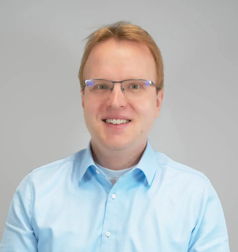 Andreas Düdder Porträtfoto von Andreas Düdder: Mann mit kurzen rötlich-blonden Haaren und Metallrahmenbrille, lächelt freundlich in die Kamera, trägt ein hellblaues Hemd, neutraler grauer Hintergrund